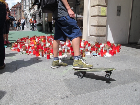 Ein Jugendlicher mit seinem Skateboard hält inne bei einer der Gedenkstätten, die in der Grazer Herrengasse mit Kerzen und Blumen entstanden sind.